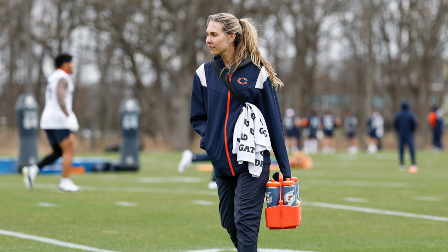 Carly Collins carries waterbottles on a football practice field