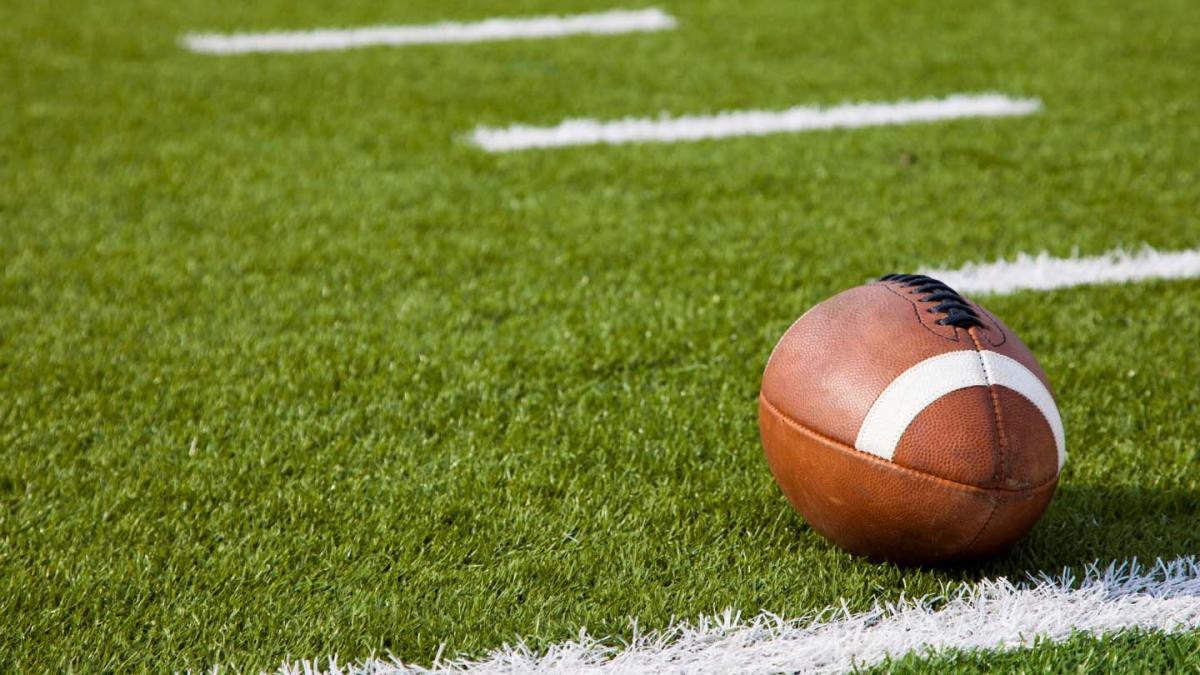 An American Football on a green grass field with white lines painted