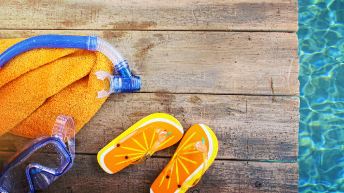 Snorkeling gear, ball and flip flops are situated next to clear and sparkling blue water